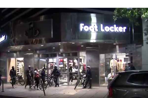 (Police standing outside the looted Foot Locker Store): Police presence outside the looted Foot Locker store.
