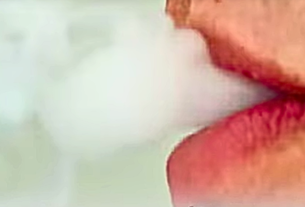 Close-up of lips inhaling smoke from an electronic cigarette, illustrating the potential risks associated with Vaping.