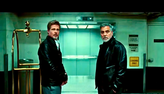 Brad Pitt and George Clooney smiling and standing together on the set of Wolfs.